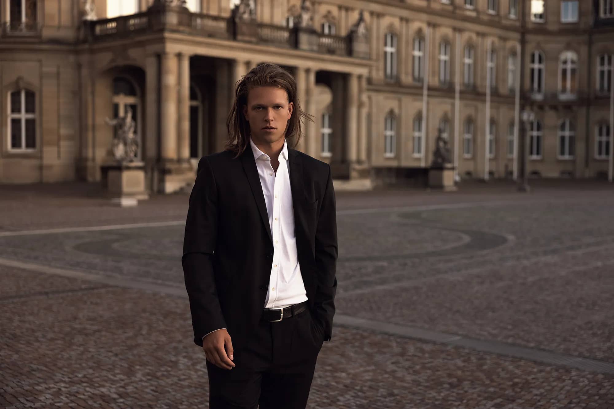 Ein eleganter Mann in Anzug vor einem imposanten Schloss.