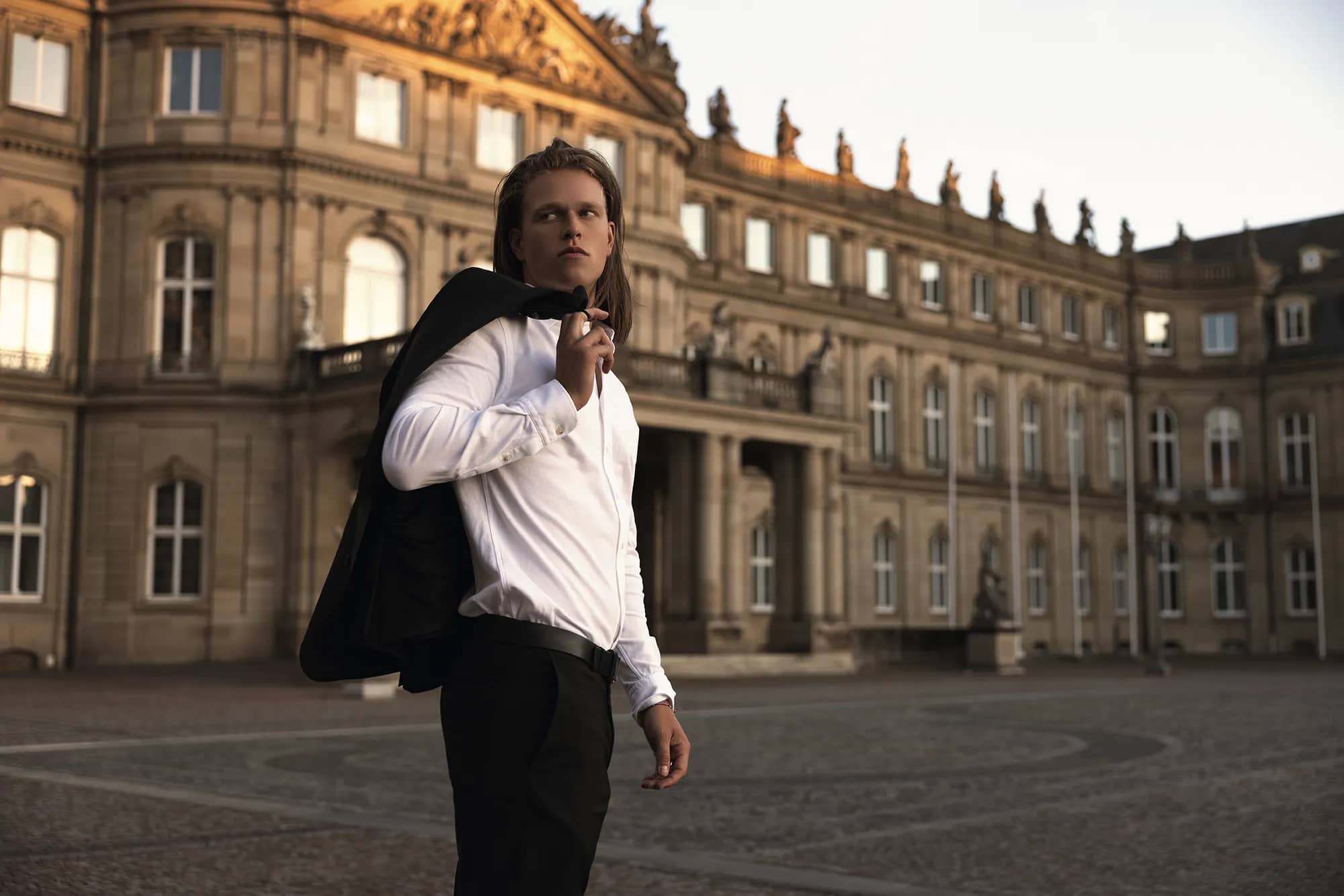 Ein eleganter Mann in Anzug vor einem imposanten Schloss.