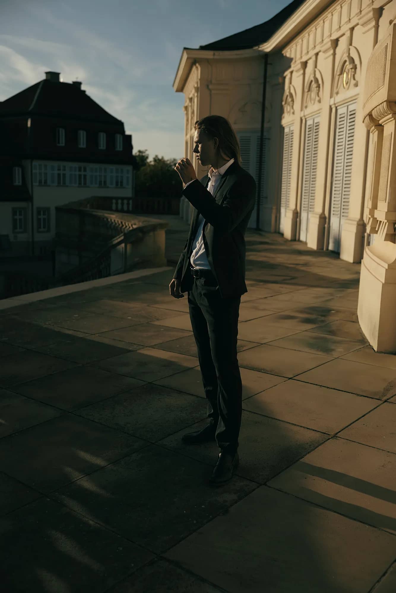 Ein Mann im Hochzeitsanzug posiert vor einem sonnigen Schloss.
