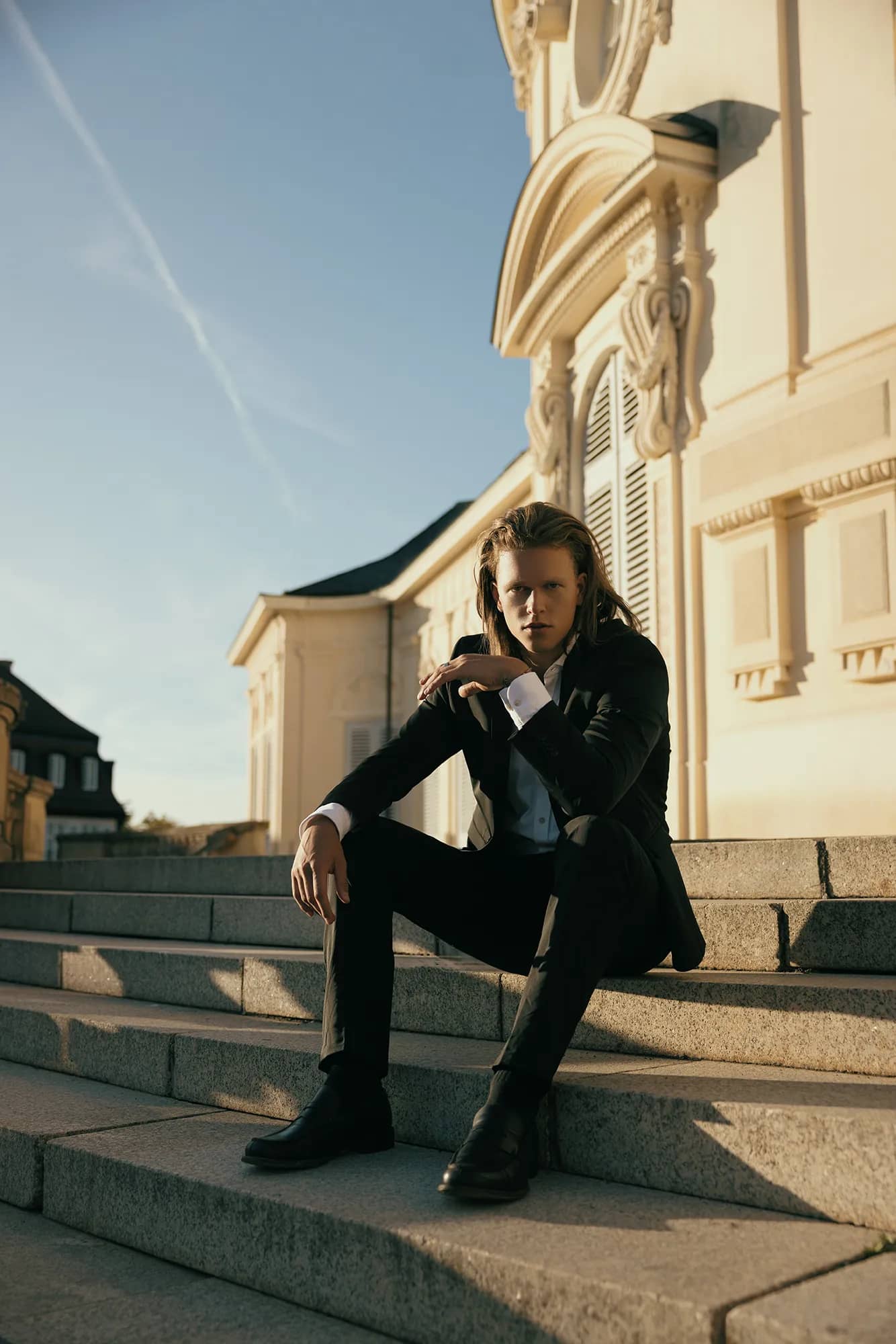 Ein Mann im Hochzeitsanzug sitzt auf einer Treppe vor einem Schloss bei strahlender Sonne.