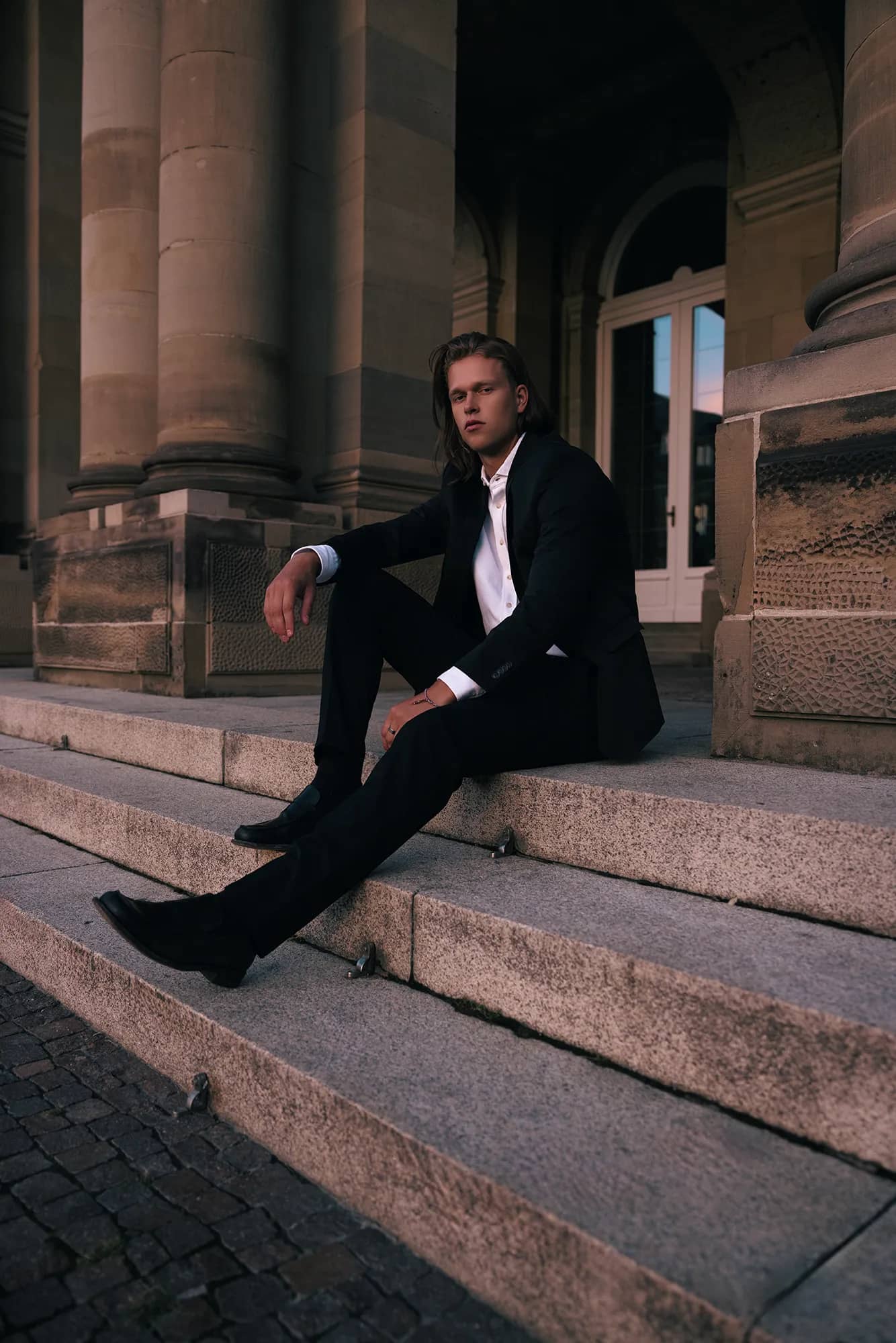 Ein eleganter Mann im Anzug posiert auf einer Treppe vor einem Schloss.
